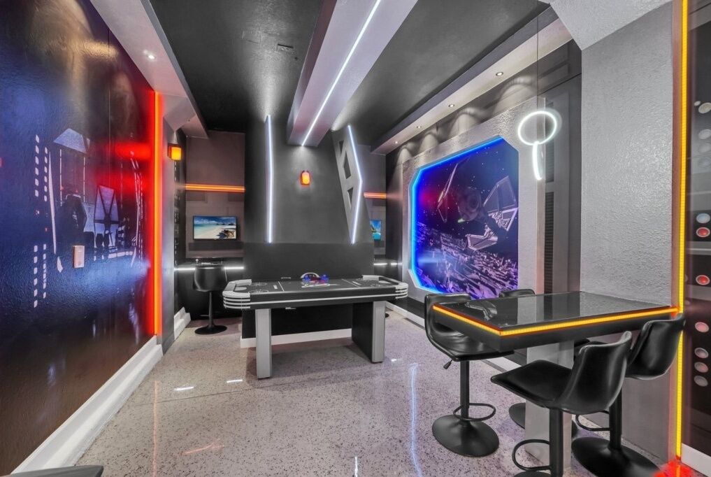 A modern room with a large screen displaying a space-themed image, a sleek black table with chairs, and a unique wall design with geometric patterns and a neon light.