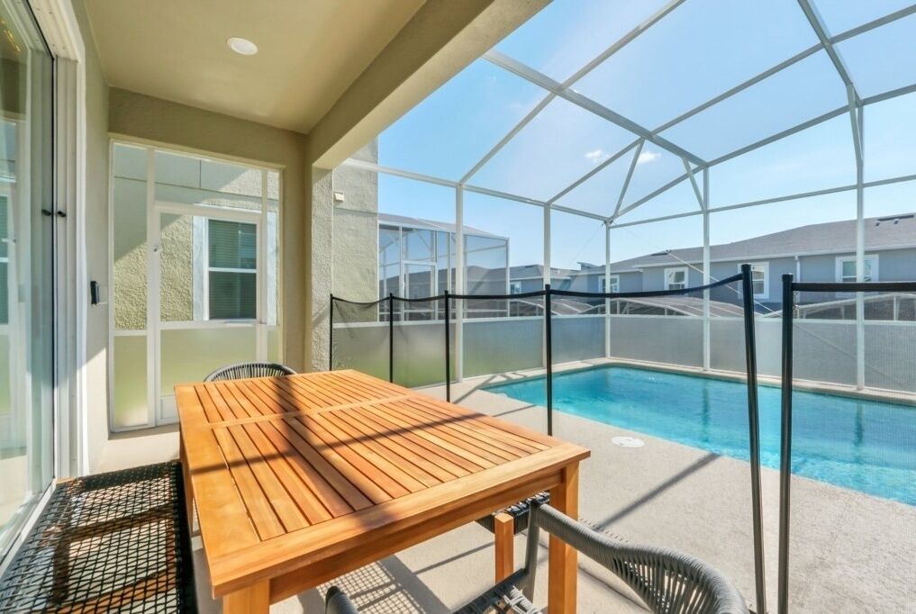 Un espacio al aire libre techado con una mesa y sillas de madera, una piscina y vistas a otros edificios.