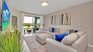 A living room with a beige sectional sofa, a patterned rug, and abstract wall art.
