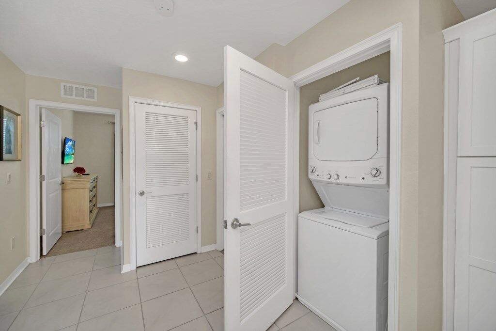 A laundry room with a front-loading washer and dryer, beige walls, and white doors.
