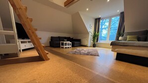Een moderne woonkamer met een houten trap, een bank, een bijzettafeltje en een potplant.