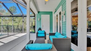 A covered outdoor seating area with wicker furniture and teal cushions, a glass door, and a view of the outdoors. - Amazing Reunion Resort 1421fair 5 Bedroom Villa (Kissimmee)