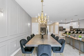 A modern kitchen with a central island, pendant lighting, and a dining area with a long table and chairs. - 4552target 9 Bedroom Home (Kissimmee)