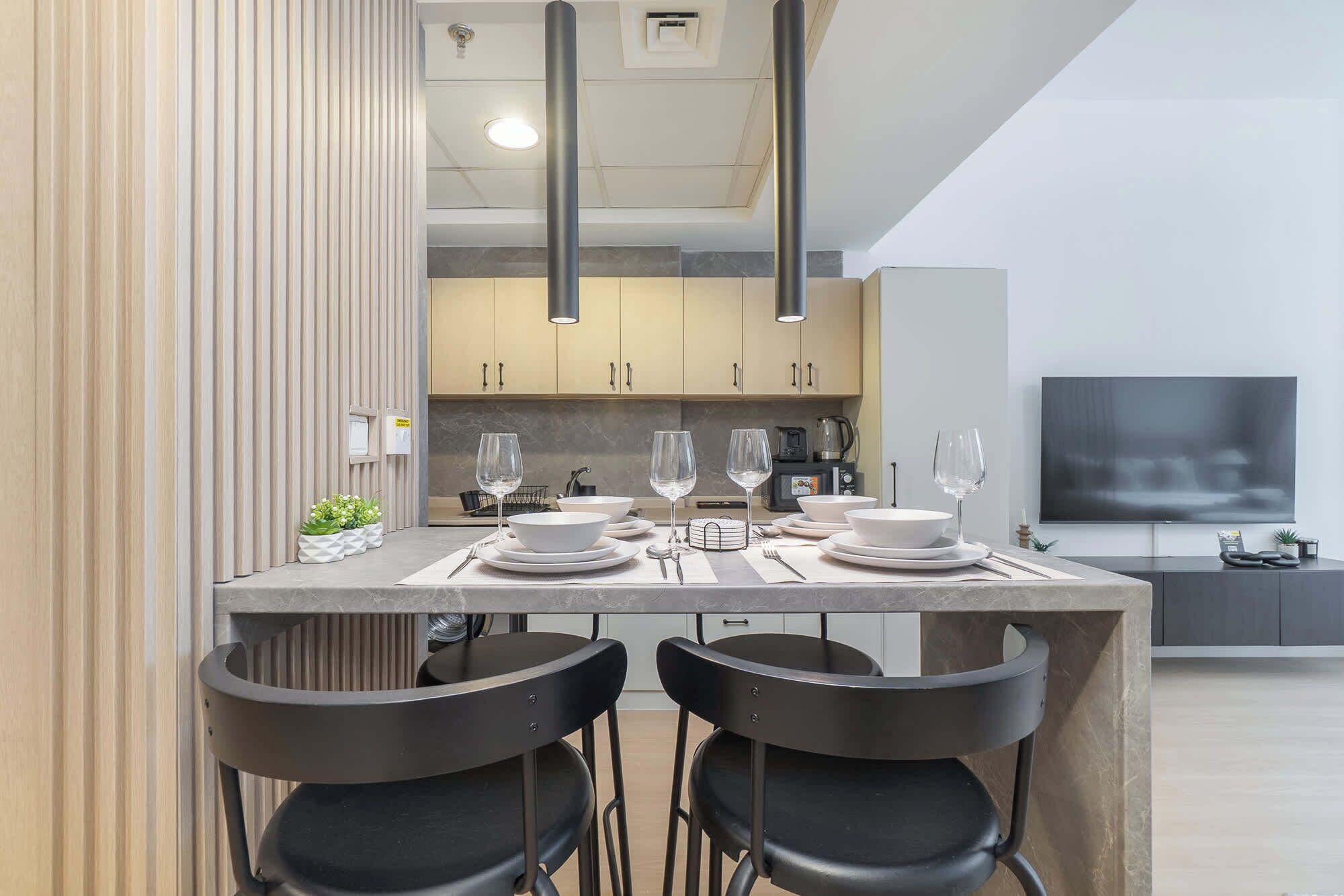 A modern kitchen with a dining area, featuring a large island with chairs, a TV, and a coffee machine.