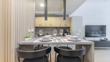 A modern kitchen with a dining area, featuring a large island with chairs, a TV, and a coffee machine.