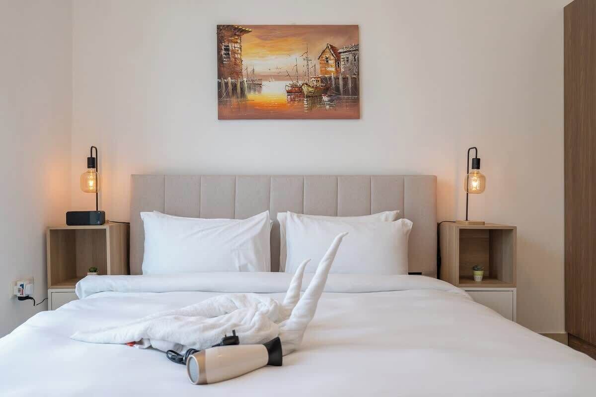 A hotel room with a large bed, two bedside tables, a painting above the bed, and two wall-mounted lamps.