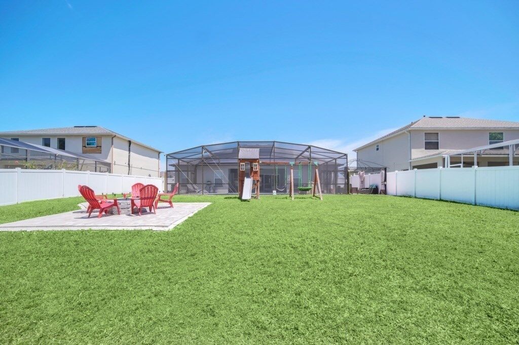 A backyard with a covered patio area, red chairs, and a lawn.