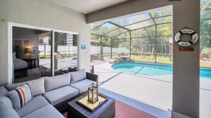 Um alpendre coberto com piscina, sofá e área de jantar.