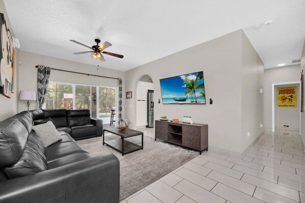 A modern living room with a black leather sofa, a coffee table, and a TV on the wall.