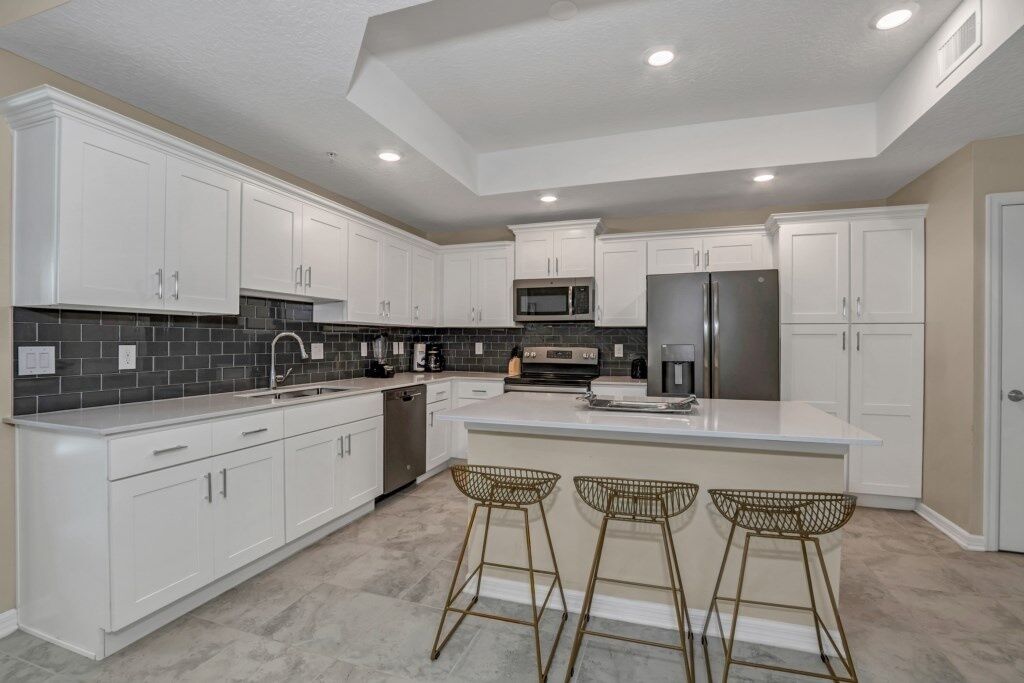A modern kitchen with white cabinets, a central island, bar stools, and built-in appliances.