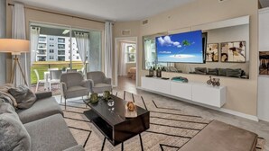 Ein modernes Wohnzimmer mit einem großen Flachbildfernseher, grauen Sofas, einem Couchtisch und einer weißen Unterhaltungsanlage mit Kunstwerken.