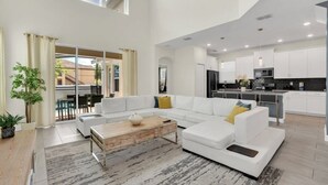 A spacious living area with a white sofa, a wooden coffee table, and a view of the kitchen in the background.