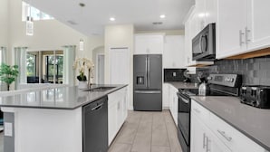 A modern kitchen with white cabinets, stainless steel appliances, and a large island.