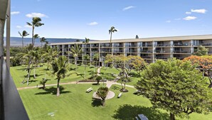 A hotel with multiple balconies, a well-maintained lawn, and palm trees. - Maui Sunset A412 1 Bedroom Condo (Kihei)