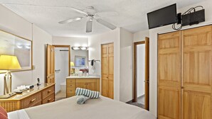 A hotel room with a bed, a desk with a lamp, a wardrobe, and a ceiling fan. - Maui Sunset A412 1 Bedroom Condo (Kihei)