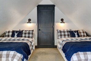 Two single beds with checkered bedding and throw blankets, flanked by wall-mounted lights.
