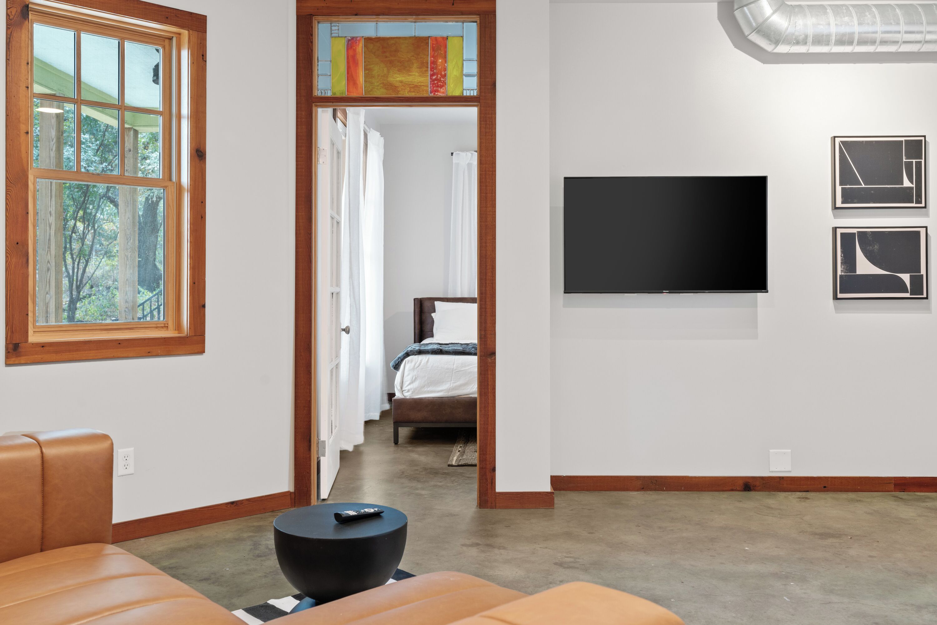 A modern living room with a large window, a flat-screen TV, and a sofa.