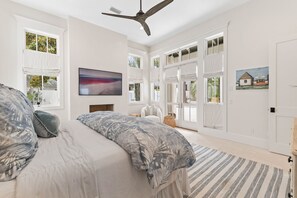 A bedroom with a large bed, a ceiling fan, and a view of the outdoors through large windows.