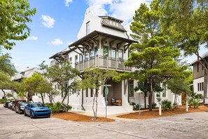 A two-story house with a balcony, surrounded by trees and parked cars.