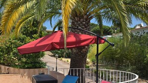 Een zwembadterras met ligbedden, een rode parasol en een palmboom.