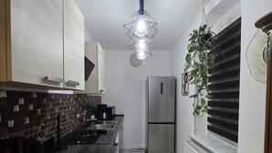 A narrow kitchen with a black countertop, a stainless steel refrigerator, a hanging light fixture, and a radiator. - Cozy, pet-friendly one-bedroom apartment in Meißen (Meißen)