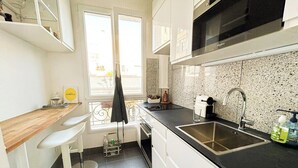 A compact kitchen with white cabinets, a black countertop, a stainless steel sink, and a window with a view of the outside.
