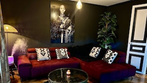 A modern living room with a red sofa, patterned cushions, a glass coffee table, and a large plant.
