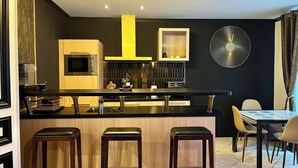 A modern kitchen with a central island, bar stools, a microwave, and a large clock on the wall.