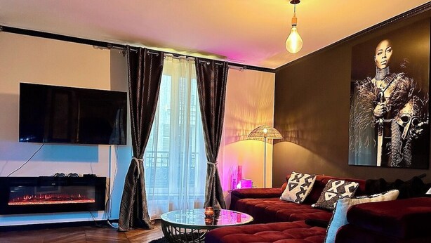 A modern living room with a red sofa, a glass coffee table, a fireplace, and a large painting on the wall.