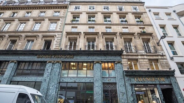 Un edifici amb els cartells 'BANQUE FRANCAISE' i 'CHANGE-OR', amb arquitectura clàssica que inclou columnes i grans finestres.
