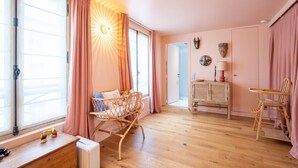 Una habitació acollidora amb bressol, cadires de vimetla, una taula petita i un armari.