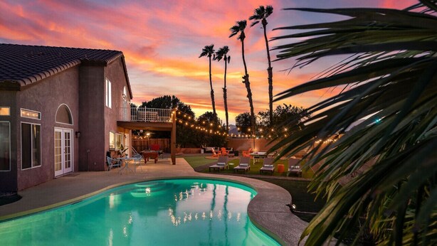 En swimmingpool med udsigt til solnedgang, en overdækket terrasse og palmer.