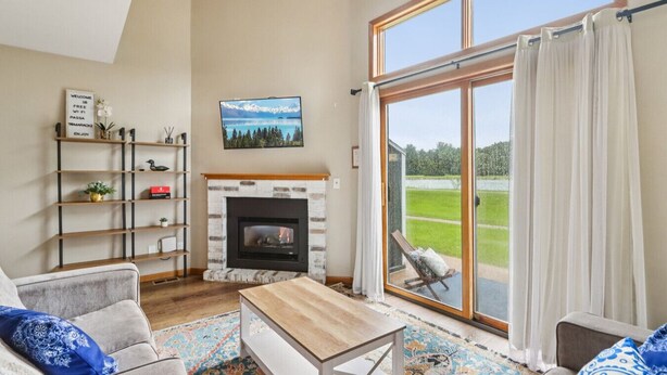 A living room with a fireplace, a large window with curtains, a sofa, a coffee table, and a bookshelf. - Waterfront Boho Retreat (Wisconsin Dells)