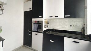 A modern kitchen with black and white cabinetry, a built-in oven, and a white tiled backsplash. - Chic Parisian Apartment in the Heart of the 17th (Paris)