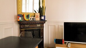 A room with a fireplace, a television, and a table. - Chic Parisian Apartment in the Heart of the 17th (Paris)