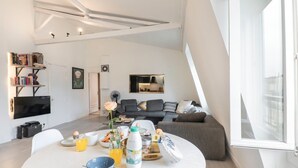A modern living room with a dining area, a sofa, a TV, and a bookshelf.