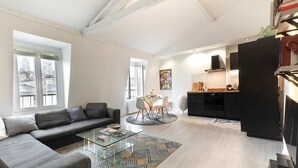 A modern living room with a sofa, a glass coffee table, and a dining area with chairs.