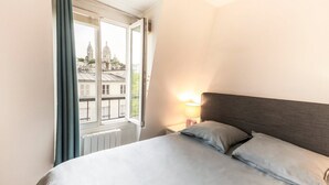 A bedroom with a bed, a nightstand with a lamp, and a window with curtains.