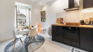 A modern kitchen with a dining area, featuring a large window with a city view, a black dishwasher, and a wooden countertop.