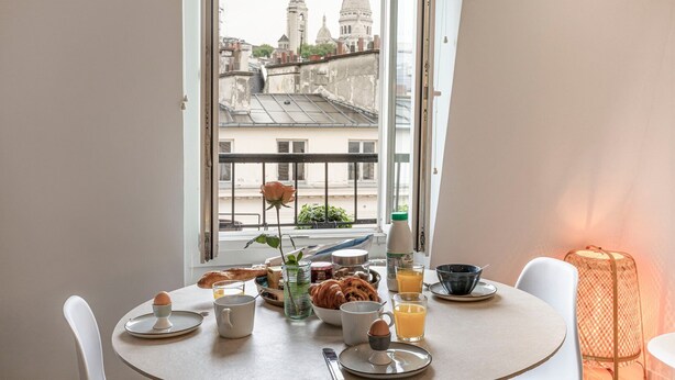 A breakfast table with croissants, eggs, and orange juice, overlooking a cityscape with domed buildings.
