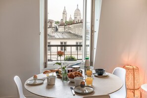 A breakfast table with croissants, eggs, and orange juice, overlooking a cityscape with domed buildings.