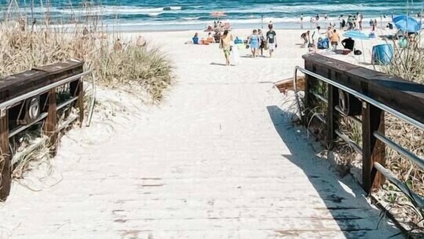 Een zandpad langs het strand dat naar de oceaan leidt, met mensen en parasols.