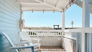 Een overdekt terras met twee Adirondack-stoelen, een pergola met lichtslingers en uitzicht op het strand.