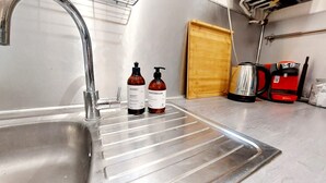 A kitchen with a stainless steel sink, two bottles of hand sanitizer, a wooden door, and a red coffee maker. - Haussmannian apartment at the gateway to Paris (Aubervilliers)