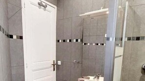 A bathroom with a white door, a sink with a mirror, and a shower area. - Haussmannian apartment at the gateway to Paris (Aubervilliers)