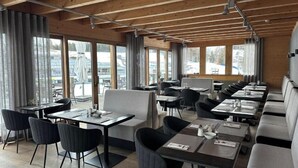 Ein modernes Restaurant mit Holzbalken, großen Fenstern und einer Mischung aus Tischen und Sitzecken.