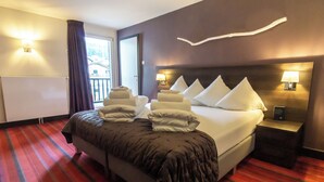 Ein Hotelzimmer mit einem großen Bett, einem Nachttisch mit Lampe, einem Fenster mit Vorhängen und Blick ins Freie.