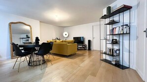 A modern living room with a yellow sofa, a dining table with chairs, a TV, and a bookshelf. - Prestigious Apartment - Faubourg Saint-Honoré (Paris)
