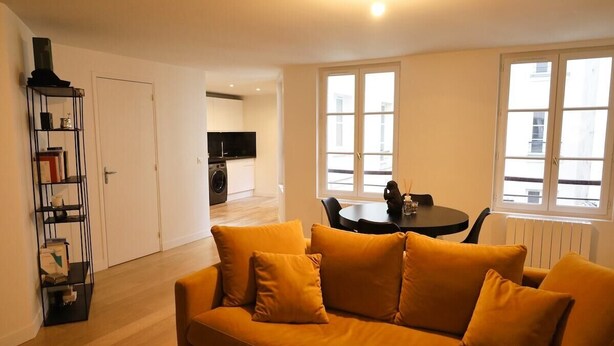 A living room with a sofa, a dining table, and a kitchen in the background. - Prestigious Apartment - Faubourg Saint-Honoré (Paris)