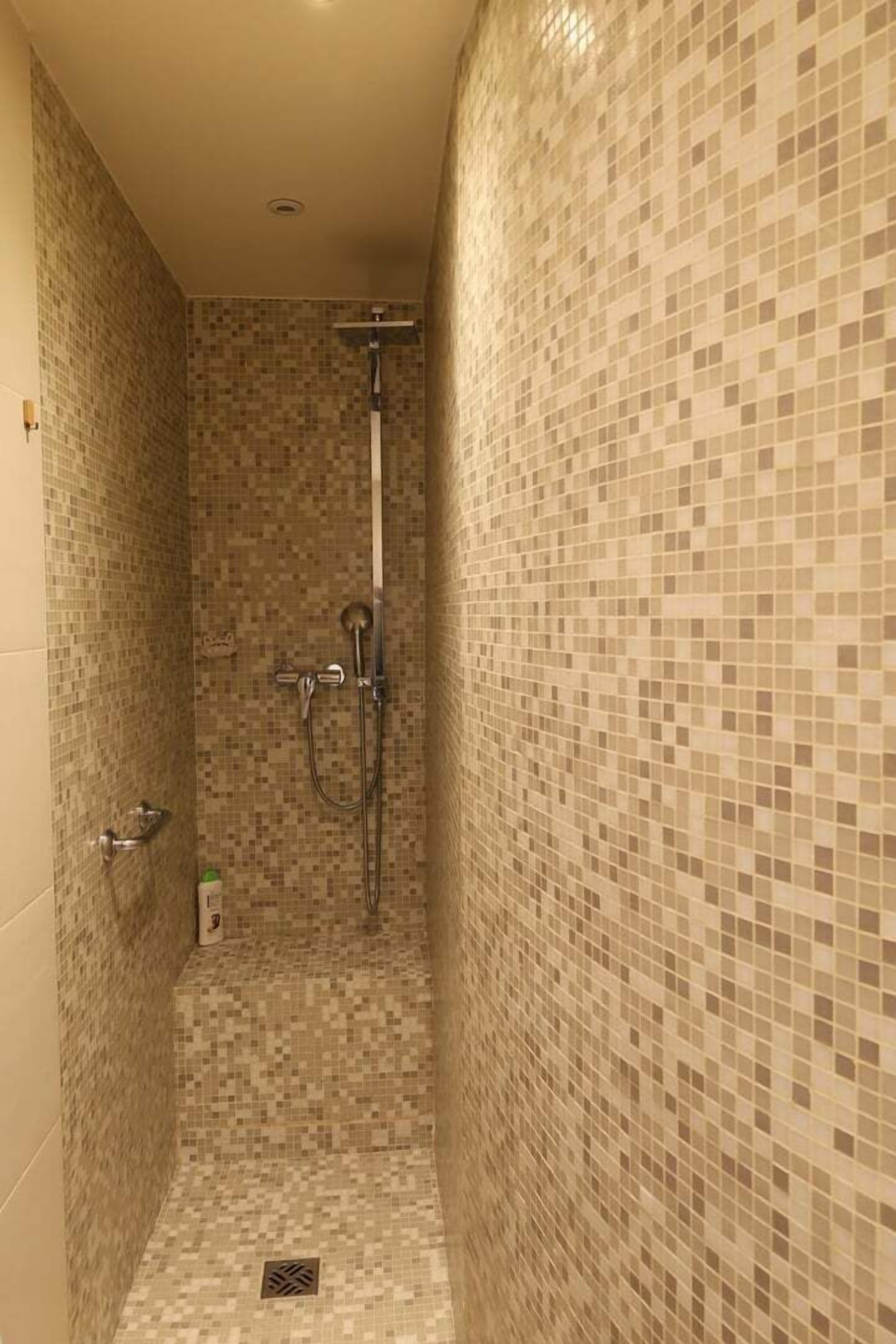 A small, tiled shower room with a handheld showerhead and a vertical rain showerhead.